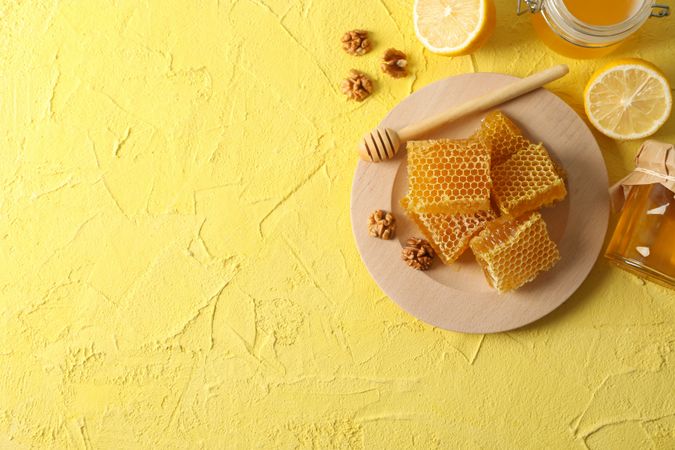 Walnut, honeycombs, jars with honey, dipper and lemon on yellow background, copy space