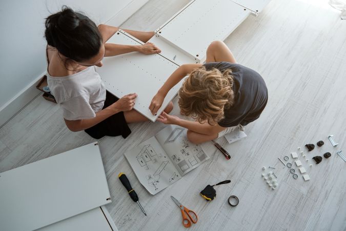 Woman and boy assembling furniture on floor in apartment