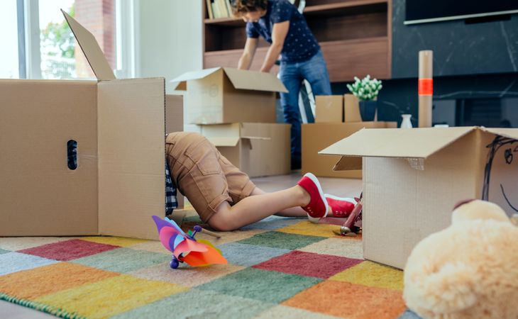 Boy playing inside a moving box while his father unpacks