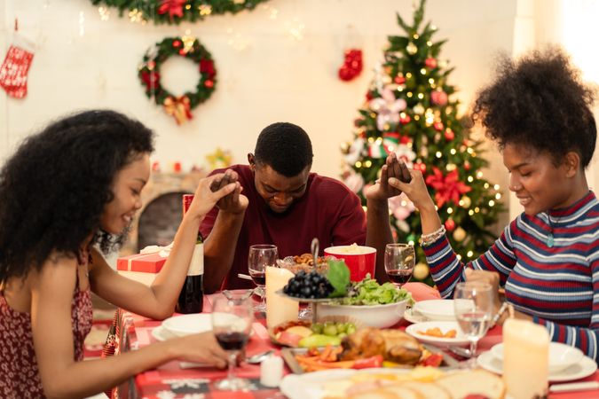 Diverse Black family holding hands, bowing heads. Praying at Christmas dinner