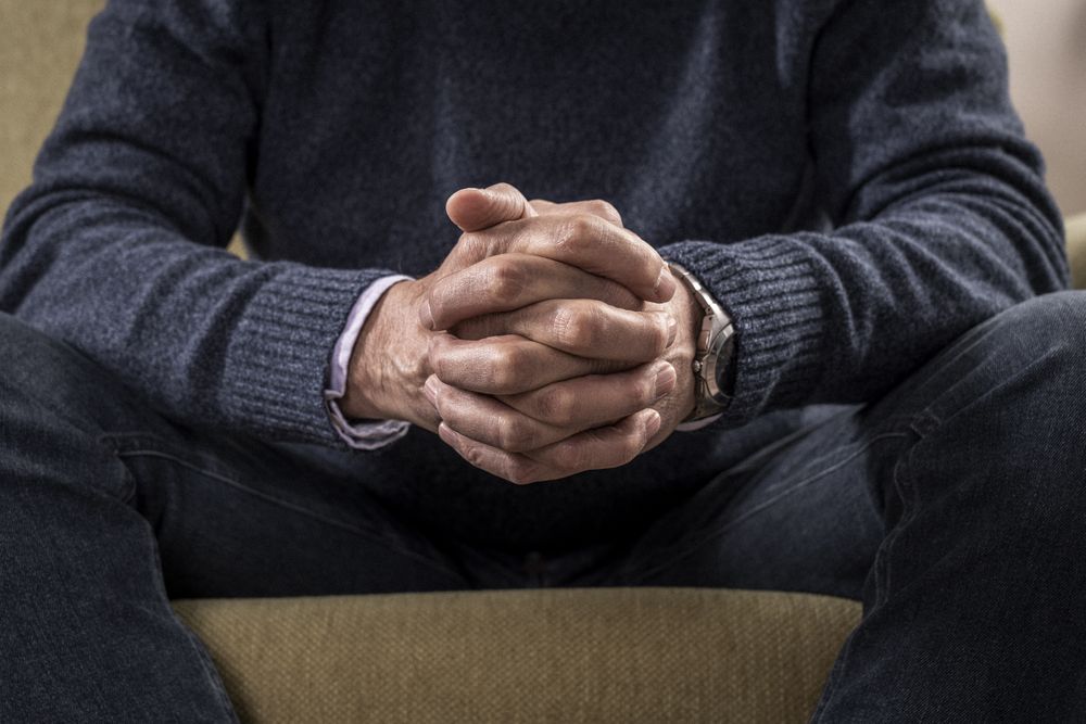 Close-up of a mature man's clasped hands on his lap.