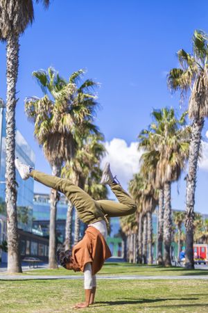 Black female doing hand stand under the palms in a promenade