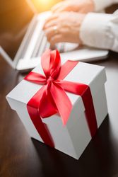 Gift Box with Red Ribbon and Bow Near Man Typing on Laptop Computer.