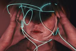 Portrait of woman with light hair holding blue led light thread in red lit studio
