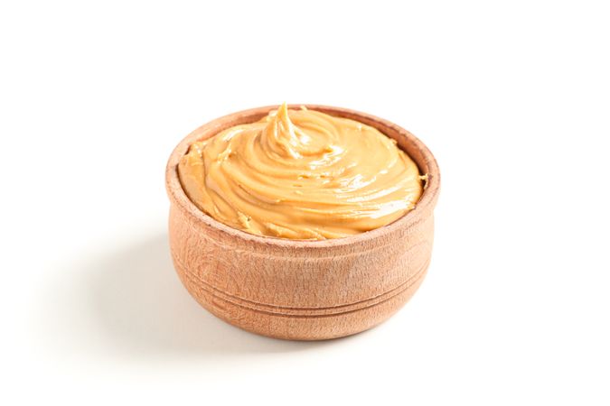Creamy peanut butter in wooden bowl isolated on light background. A traditional product of American cuisine