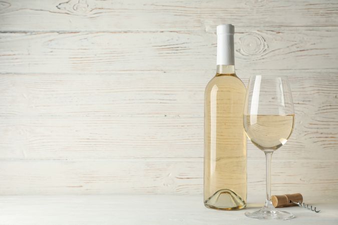 Corkscrew, bottle and glass with wine on blank wooden background, copy space