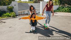 Smiling girl pushing her friend who is sitting on a longboard from behind 499NW4