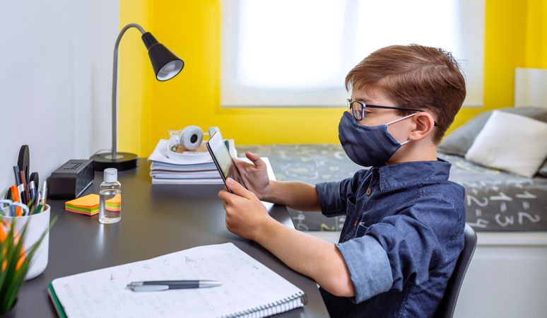 Boy with face mask doing homework with a tablet