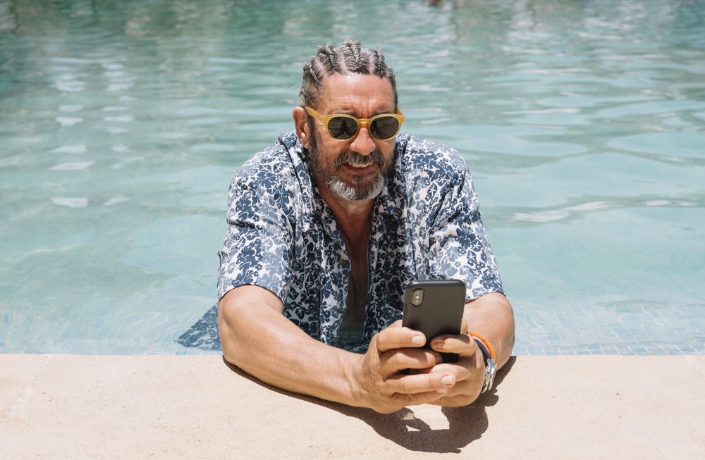 Grey haired man using smartphone in swimming pool