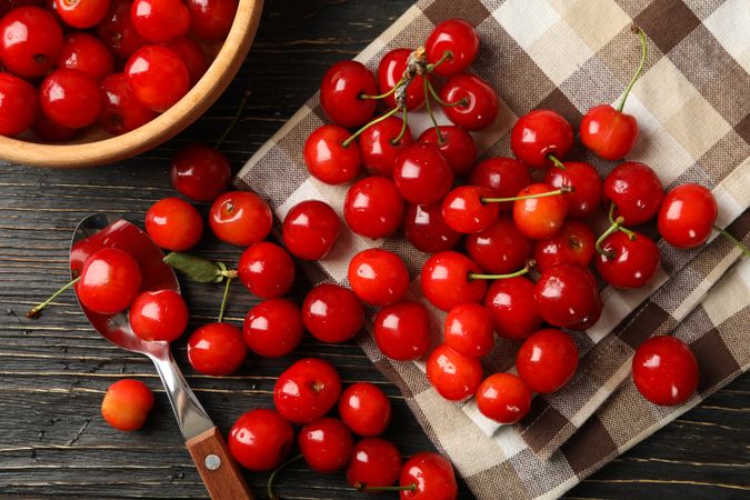 Towel, spoon and bowl with cherry on wooden background, top view