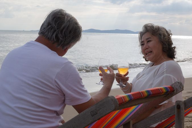 Mature Asian couple relaxing on the beach and toasting with wine