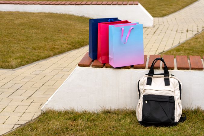 Three shopping bags and backpack placed outdoors in park.