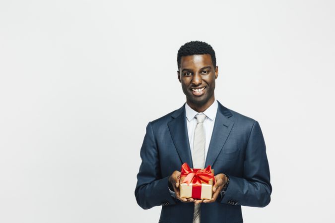 Happy Black man presenting present wrapped in gold paper with red bow