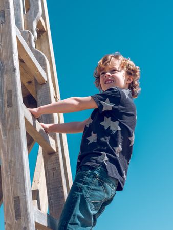 Delightful child standing on wooden ladder of playground