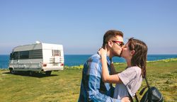 Couple kissing near the coast with a camper