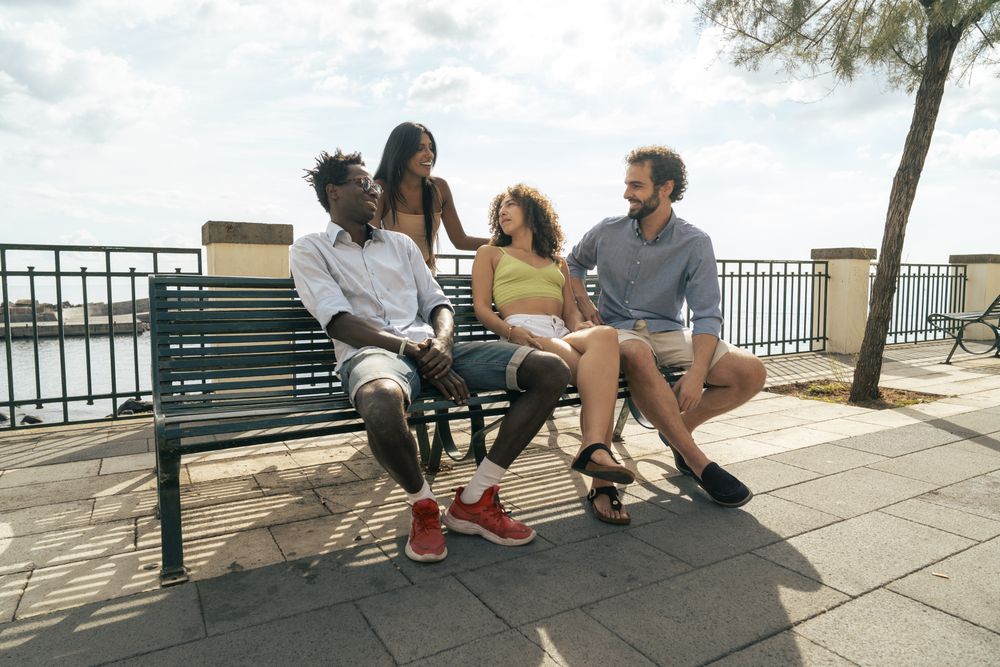 Group of young multicultural friends talking on a bench by the sea.