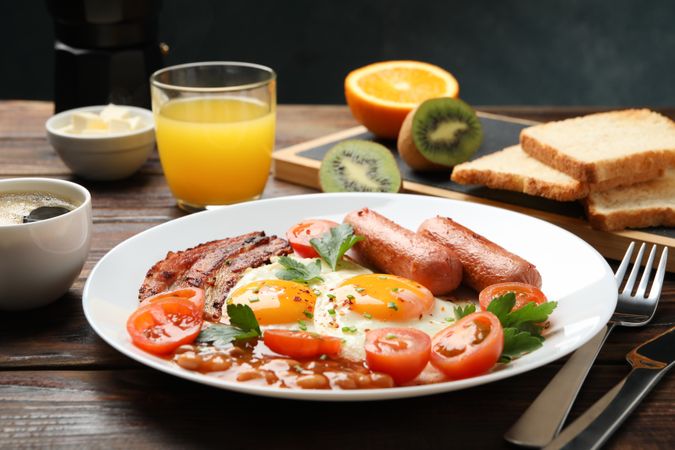 Wooden table with breakfast plate of eggs, tomatoes, sausage and bacon