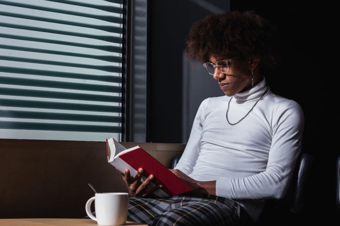 Relaxed young Black man reading book in street cafe