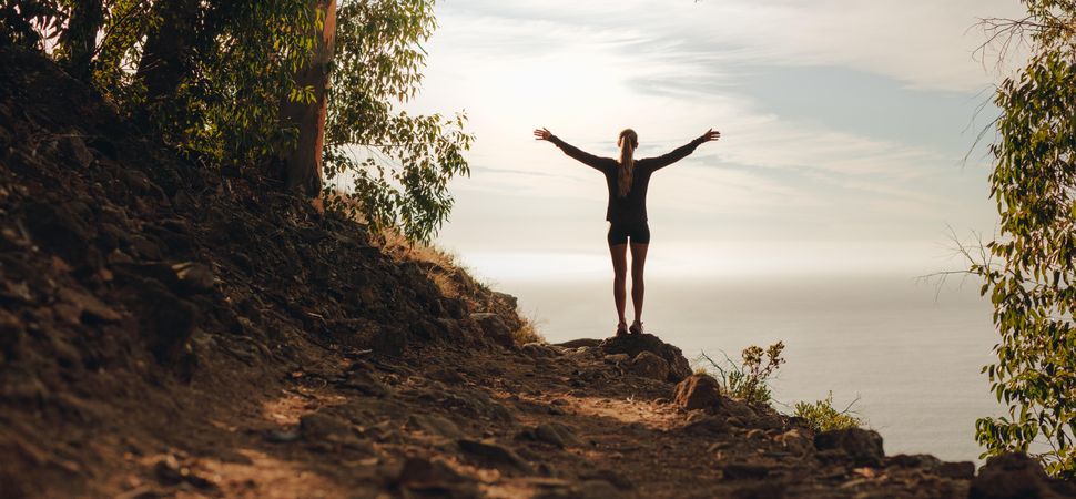 Female runner with arms outstretched on mountain peak