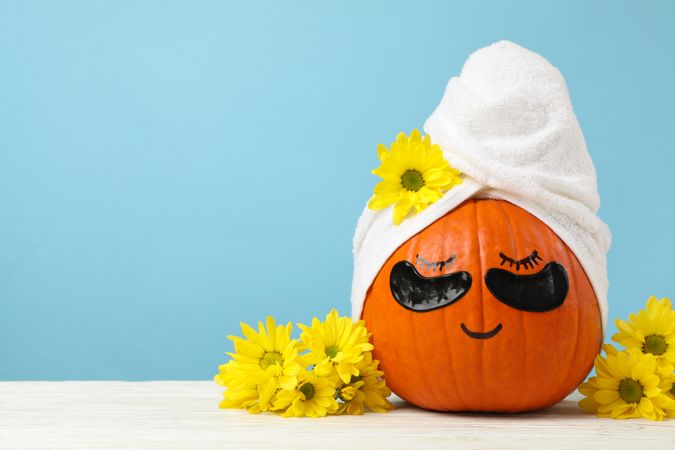 Pumpkin with towel, flowers and under eye patches against blue background