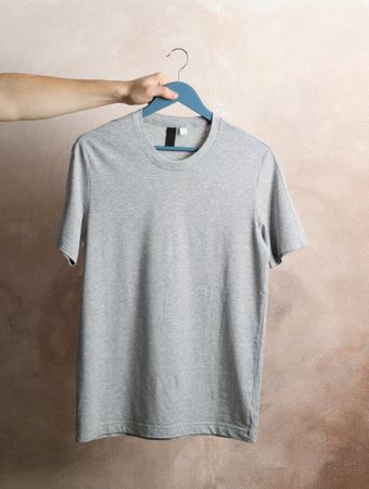 Man holds a hanger with blank gray t-shirt on brown background, space for text