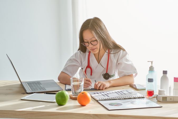 Focused Asian doctor writing at table in medical room