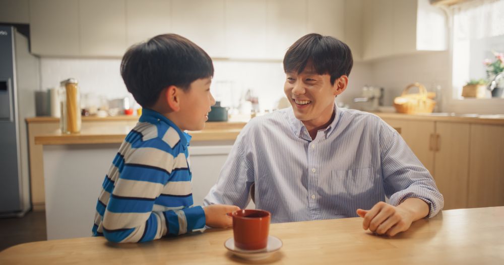 Portrait of Fatherly Love: Korean Young Man and his Son Talking, Joking Around, Bonding Together While Sitting at Home.