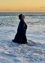 Young man standing in waves at the beach at sunset