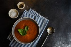 Grey bowl of gazpacho soup with basil leaves on striped napkin with copy space