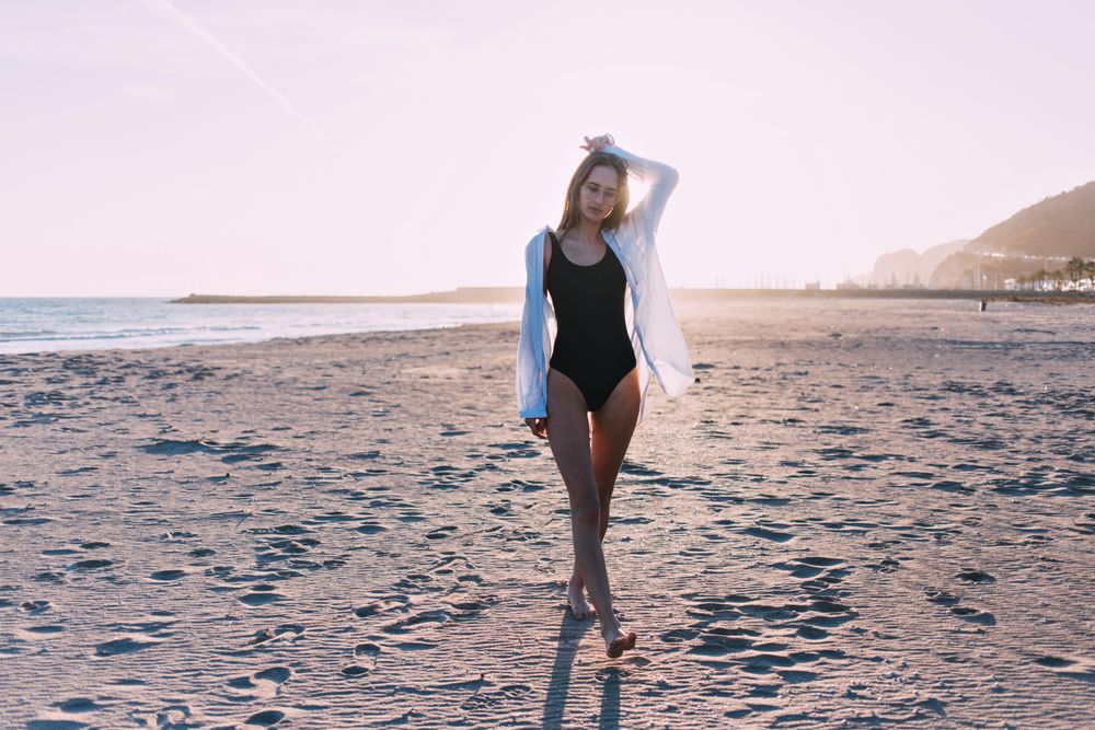 Young woman standing on beach with sunset at her back holding her hair