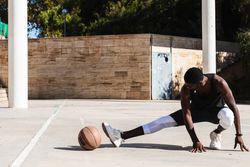 Black sportsman stretching on basketball court