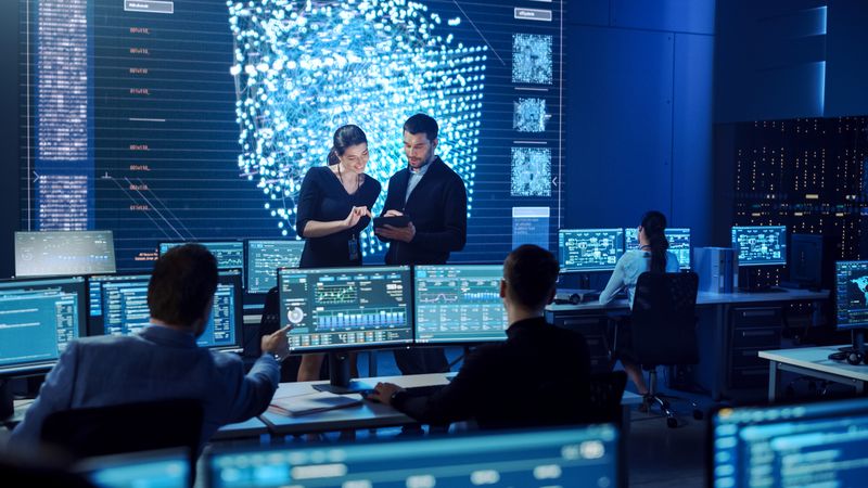 In a High-tech Control Room, a Diverse Team Collaborates on Data Analysis, Focusing on a Tablet