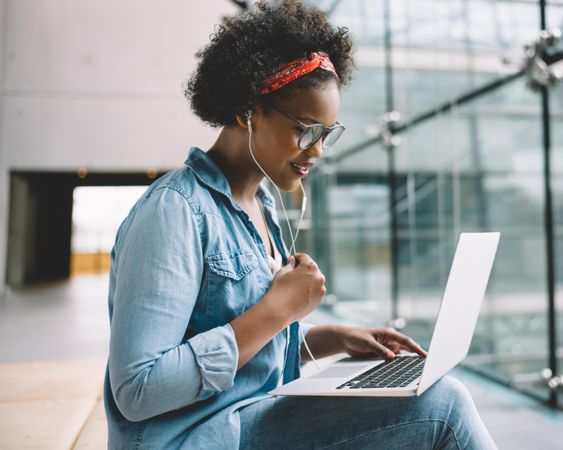 Woman sitting with laptop wearing earbuds