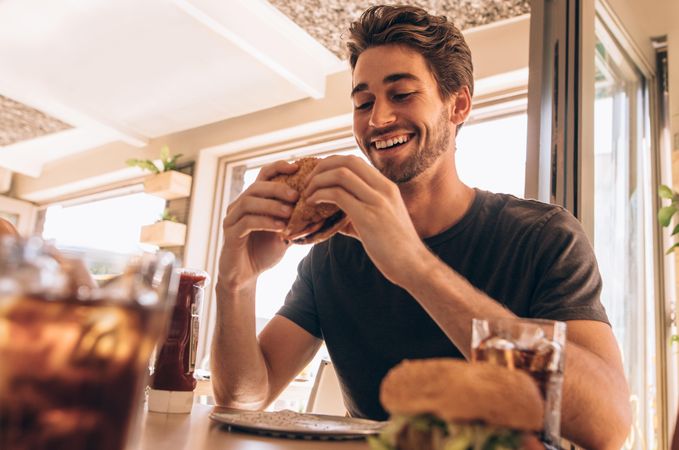 Happy young man eating a delicious burger at restaurant