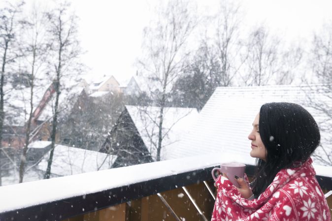 Woman with drink and blanket under snowfall