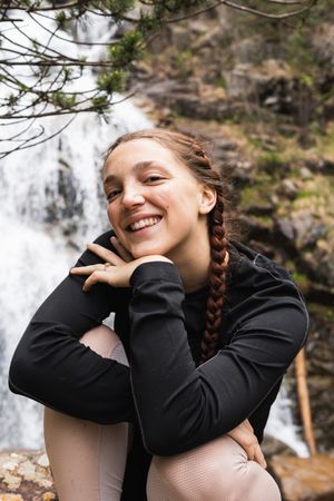 Delighted traveling woman looking at camera against waterfall