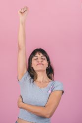 Happy woman wearing a pink breast cancer awareness ribbon is raising her arm showing the struggle with breast cancer