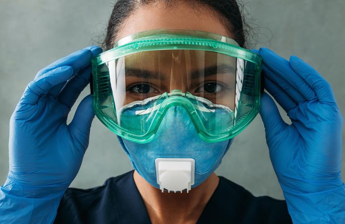 Female Black doctor’s face in PPE gear as she adjusts her eye wear