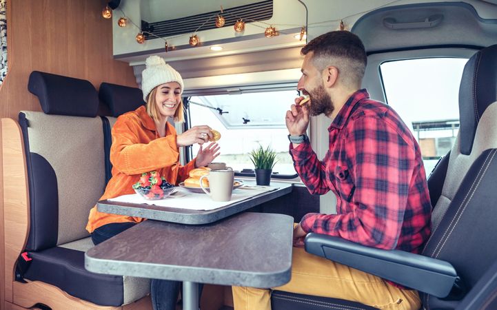 Male and female friend enjoying breakfast rolls and coffee in back of van