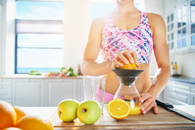 Fit woman juicing an orange in her bright kitchen