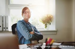 Confident female entrepreneur in jean jacket sitting at her desk in bright office 0LGorb