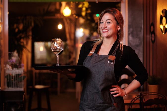 Cheerful waitress holding tray with wineglasses