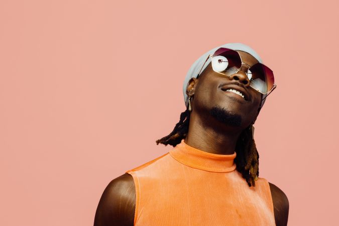 Portrait of a happy young man with sunglasses and cap laughing, isolated on pink