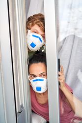 Mother with son in protective masks looking out window