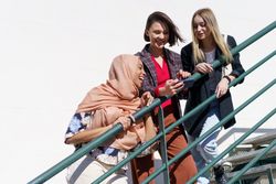 Multi-ethnic women friends, in stylish outfit and hijab looking at phone on outdoor staircase