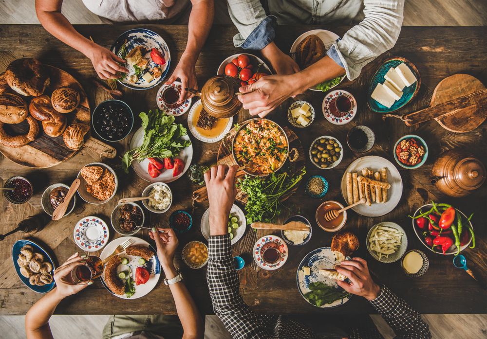 Group of people serving themselves tea and food at Turkish breakfast with eggs, breads, vegetables