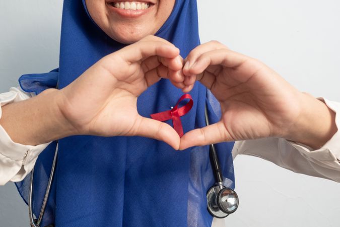 Happy Muslim Female Asian doctor or nurse hand in love or heart with Red ribbons, HIV awareness concept, world AIDS day, world cancer day.