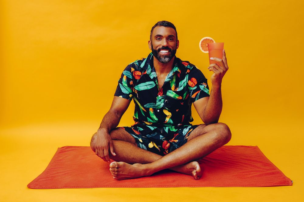 Black male sitting on towel and holding up tropical drink