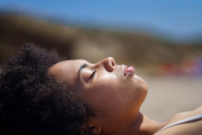 Female with curly hair relaxing with eyes closed on beach