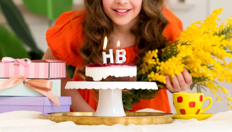 Girl smiling behind birthday cake with "HB" candles